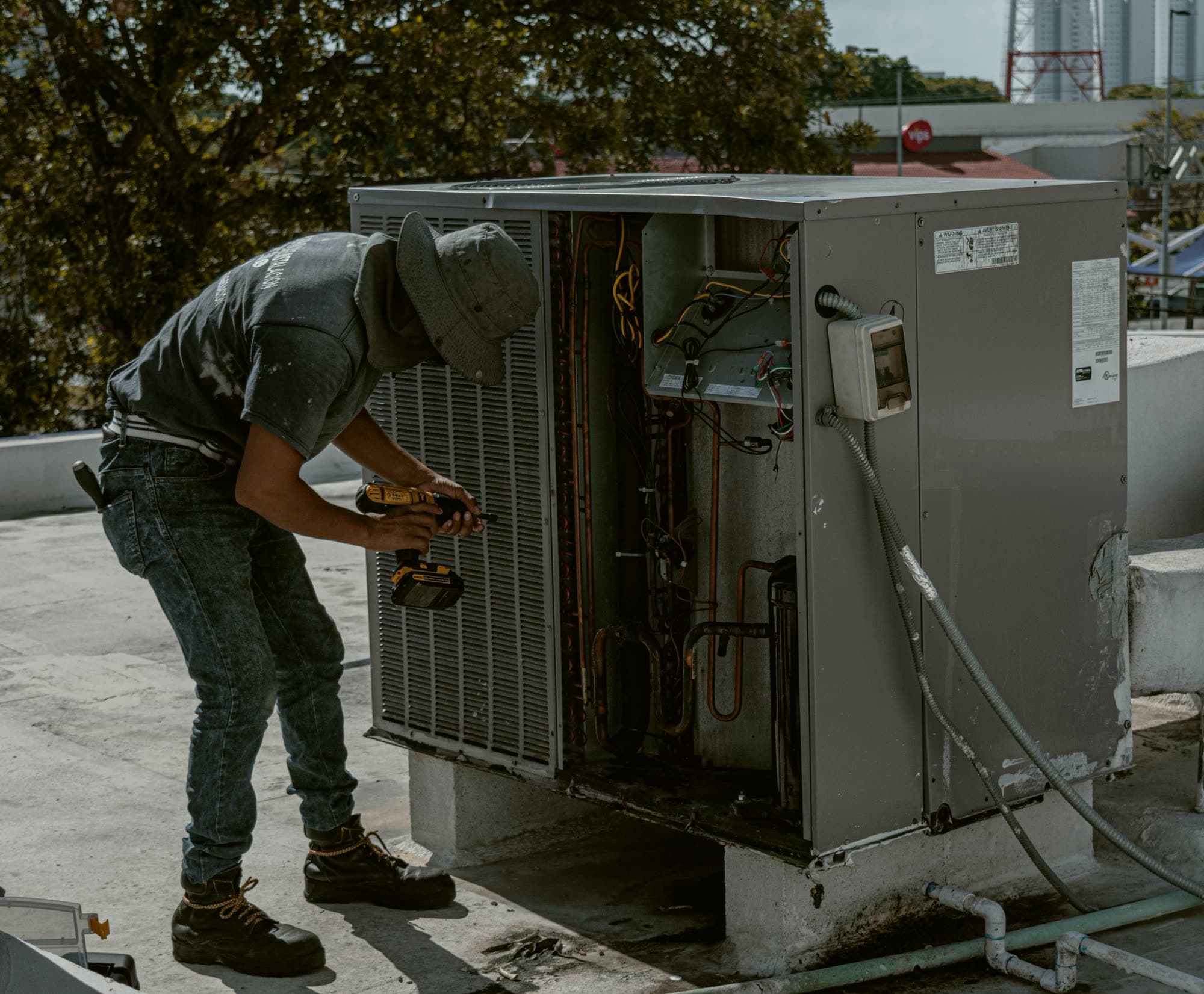 An HVAC technician repairing an outdoor air conditioning unit on a roof.